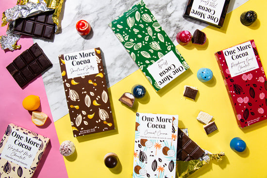 A variety of One More Cocoa chocolate bars and bonbons on a colourful backdrop